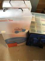 Two frosted plastic packaging boxes labeled “Knitter’s Tote,” clear plastic organizer with thread spools, and a blue zippered tote