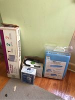 Photo showing boxed laundry sorter, Smart Living steamer, Windmere shaver, and packaged ironing board.