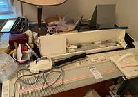 Wide view of knitting machine on table with carriage, motor drive unit, Wahl trimmer, weights and small parts in box