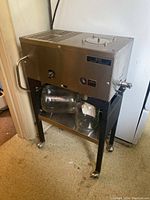 Front and side view of stainless steel distiller on stand with two glass bottles on shelf