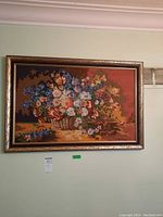 Full view of framed needlepoint artwork featuring a colorful floral basket hung on light green wall