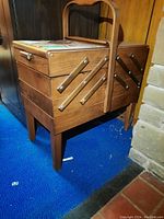 View of the closed wooden sewing box showing the cantilever design and sturdy handle on a blue carpeted floor.