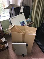 Various sewing rulers, grid marker board and cardboard box with extension table packaging, displayed upright with some leaning by window