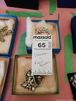 Photo of two vintage brooches in cushioned boxes with MaxSold auction tag indicating Sherman and Robert brooches