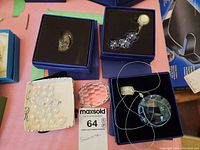 Collection view of Swarovski and unmarked mini crystals including pink and clear faceted crystals, swan figurine, and blue crystal jewelry pieces in black boxes.