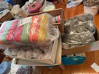 View of three boxes with yarn bundles in various colors and a box of knitting needles on wooden floor.