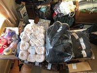 View of multiple yarn cones and skeins on table including large beige and black cones in plastic packaging.