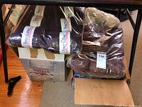 Two large plastic bags filled with yarn in dark blue and brown colors atop a cardboard box labeled Aberfoyle Spinney on a wooden floor