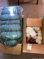 Two boxes with yarn including large green skeins wrapped in plastic and smaller mixed color skeins in one box