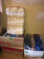 Three boxes stacked; top box shows cream-colored yarn packaged in plastic