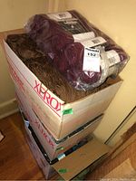 Three stacked boxes of yarn, top box with burgundy yarn skeins in plastic wrap and brown yarn skeins inside.