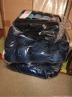 Stack of four bags with yarns in black and blue colors tightly sealed in plastic.