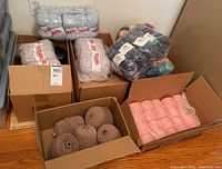 Five boxes containing assorted yarn skeins and spools of various colors and brands placed on the floor near an electrical outlet.