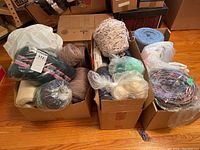 Three boxes of yarn and thread in various colors and textures, including skeins and balls of yarn, some in bags.