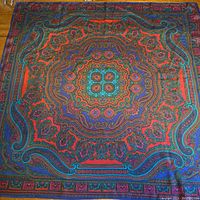 Full view of silk scarf showing rich jewel colors and detailed paisley design with central turquoise motif and vibrant red and blue borders.