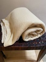 Soft butter cream wool blanket folded and rolled on wooden surface, showing overall color and texture.