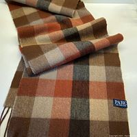 Full view of the folded PARC wool scarf showing the checkered pattern in brown, orange, and beige tones and the brand label.