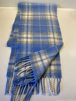 Full view of periwinkle blue and cream checkered wool scarf with fringed ends folded in half.