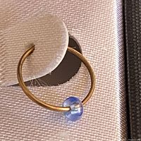 Close-up of single 10K gold hoop earring with small translucent blue bead showing hoop detail and bead.