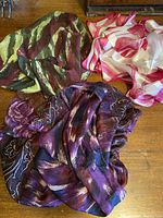Top view of three silk scarves laid out on a wooden surface showing textural details and colors.