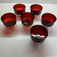 Six cherry red glass dessert bowls with clear stem and foot arranged on a white surface.
