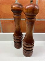 Front view of both tall wooden grinders made of maple with rounded tops and carved rings near base.