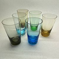 Set of 6 thin blown colored glasses arranged in a loose circle showing side profiles and color variations including amber, green, blue, chocolate, grey, and turquoise.