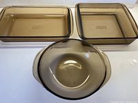 Top view of the three dishes showing rectangular, square, and round handled bowl dish all in smoky brown translucent glass with PYREX mark.