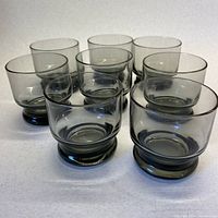 Eight smoky grey scotch glasses shown together arranged in two rows, demonstrating stackability and uniform shape.