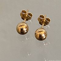 Pair of round gold hollow sphere stud earrings with polished finish shown together with backstoppers, reflecting light well.