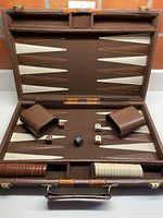 Full view of the vintage backgammon game open inside brown carrying case showing board, playing pieces, dice, dice cups and doubling cube.