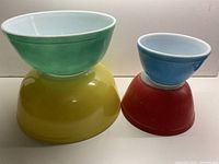 Four nesting Pyrex mixing bowls stacked two by two showing vibrant primary colors and white interiors.