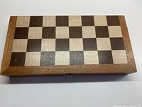 Closed wooden folding chess board with dark and light wood squares and frame.