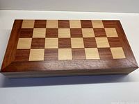 Closed wooden chess board showing alternating light and dark wood inlaid squares and framing border.