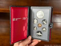 Open display case showing 7 coins, including large silver dollar commemorating National Parks Centennial and 6 smaller coins.