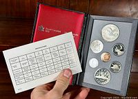Open red leather case holding 8 Canadian proof coins arranged in foam (2 dollar, quarter, dime, nickel, penny, half dollar, five cent) along with specification sheet.