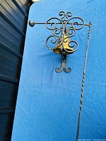 Full view of 19th century brass bell mounted in decorative wrought iron frame with pull chain and counterweight rod on blue background.