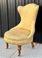 Front angle view of the yellow Victorian slipper lounge chair, showing fabric pattern and wood legs.