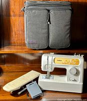 Full view of the sewing machine, foot pedal, small ironing board, and carrying case placed on a wooden surface.