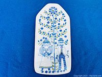 Full view of ceramic board showing entire floral design with man and woman figures and leafy branches in blue and green on white background.