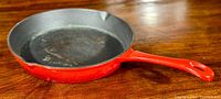 Red ceramic cast iron enamel pan with visible use marks inside, photographed on wooden surface from two angles.