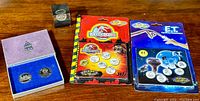 Lot display showing Hamilton 150th anniversary coin set, Jurassic Park and E.T. Royal Canadian Mint coin sets still in packaging, and small box likely containing additional coin or collectible.