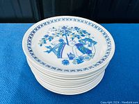 Stack of ceramic plates showing top plate with blue and green floral and folk art design under a tree.