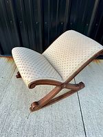 Side angled view of the rocking foot rest showing wooden frame and patterned beige fabric upholstery.