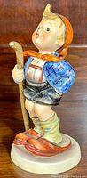 Side view of vintage Hummel Little Hiker figurine showing boy with walking stick and large slippers.