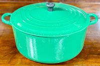 Front-right perspective of green enameled Dutch oven with lid on wooden surface