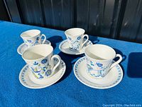 Four tea cups and matching saucers set on a blue table, shown from a front angle in sunlight to capture color and design details.