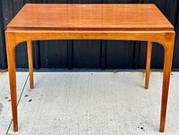 Full front view showing the entire teak wood table with tapered legs and rounded edges.