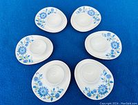 Six white ceramic Figgjo Flint Turi designed egg cups arranged in a circle, showing blue floral patterns on each.