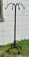 Full view of the black wrought iron plant hanger stand showing tall vertical pole and four curved arms at the top for hanging plants.